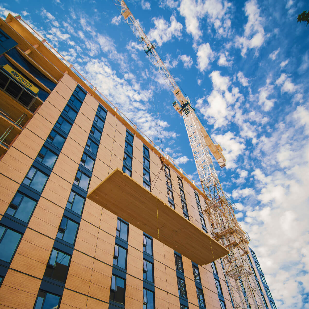 looking up at a tall beige building with a crane on top, framed against a blue sky